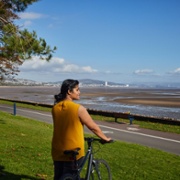 A woman stands holding a bike and looks out to sea.