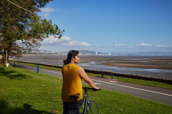 A woman stands holding a bike and looks out to sea.