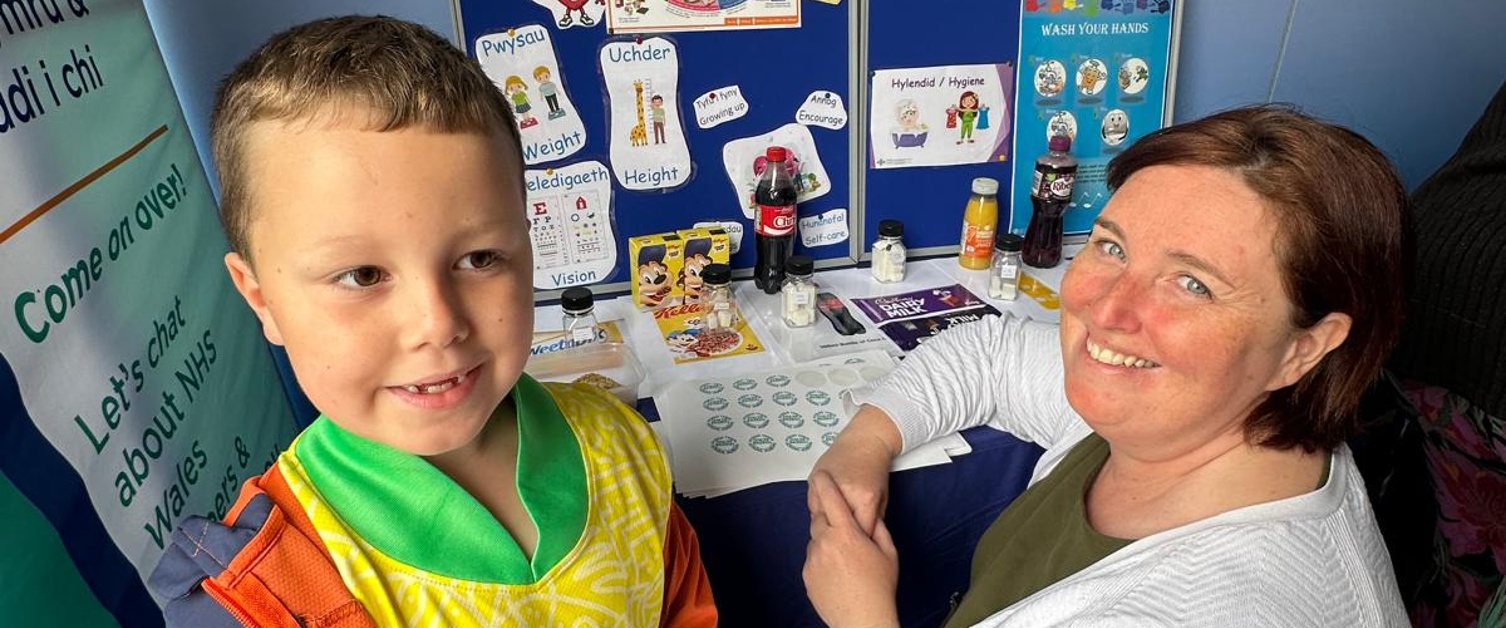 An image of a young boy and a woman smiling at the camera, stood in front of a school nursing display stand.