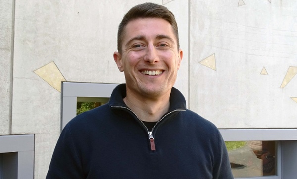 Image shows a man standing outside a hospital building and smiling into the camera