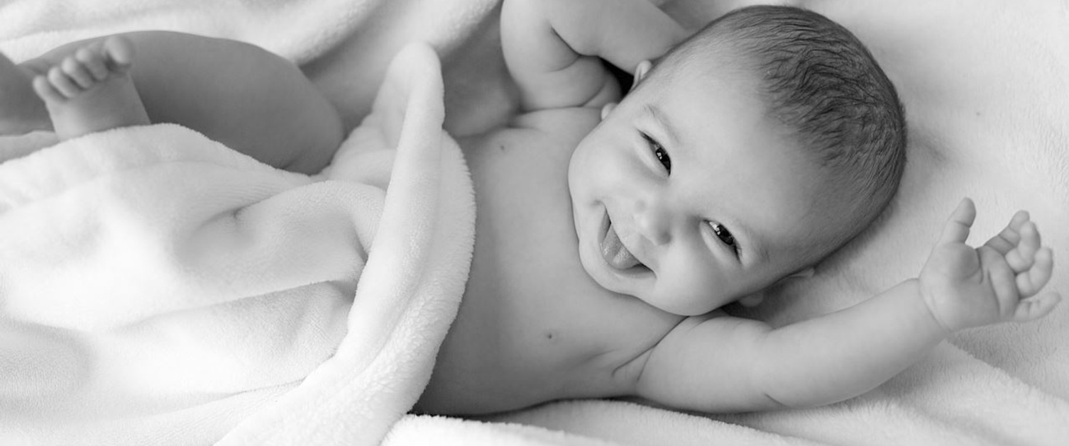 A baby wrapped in blankets smiles at the camera, appearing to laugh.