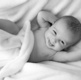 A baby wrapped in blankets smiles at the camera, appearing to laugh.