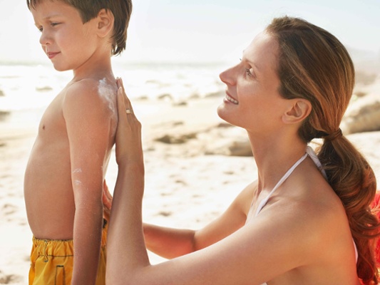 Image shows a woman applying sun lotion to a boy