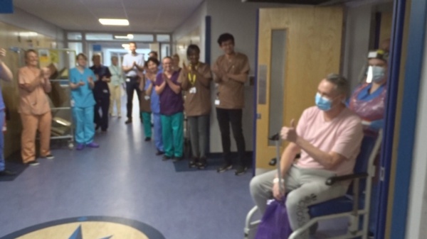 Image shows patient David Courtney-Williams giving the thumbs up to clapping staff.