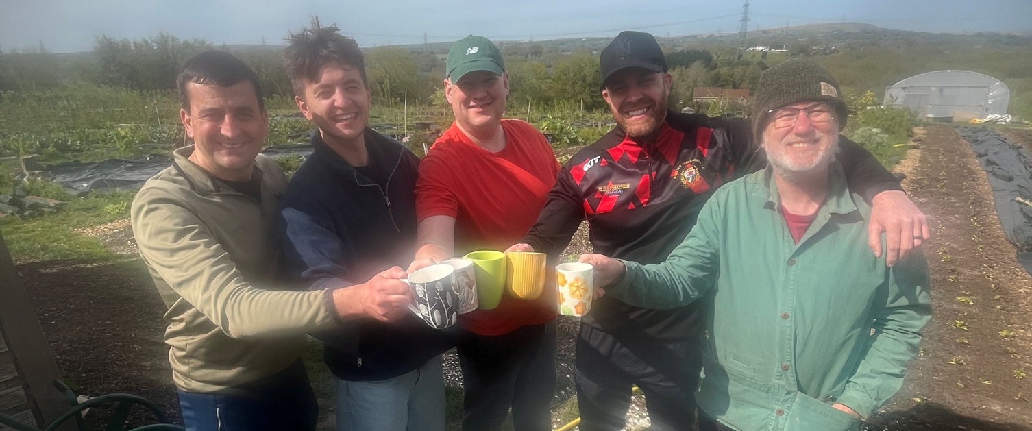 Image shows a group of men holding mugs in a field
