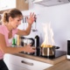 Image shows a saucepan on fire on the hob. A woman is panicking.