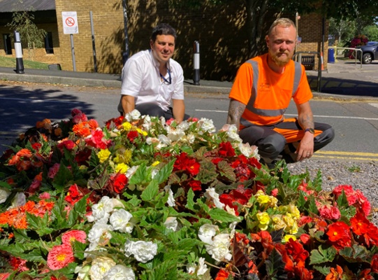 Image shows two men in front of a flower bed