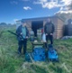 Image shows two men stood in front of a shed holding tools