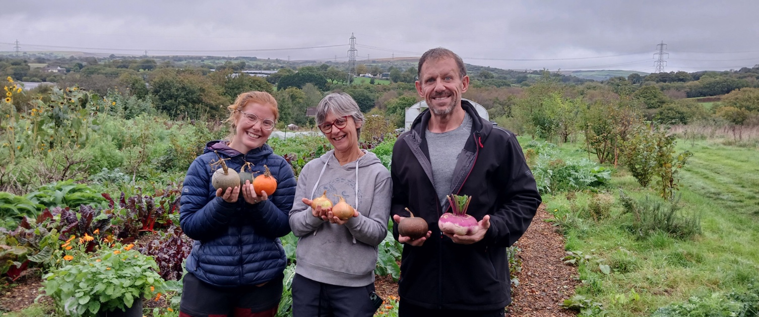 Three people holding a variety of vegetables picked at a farm