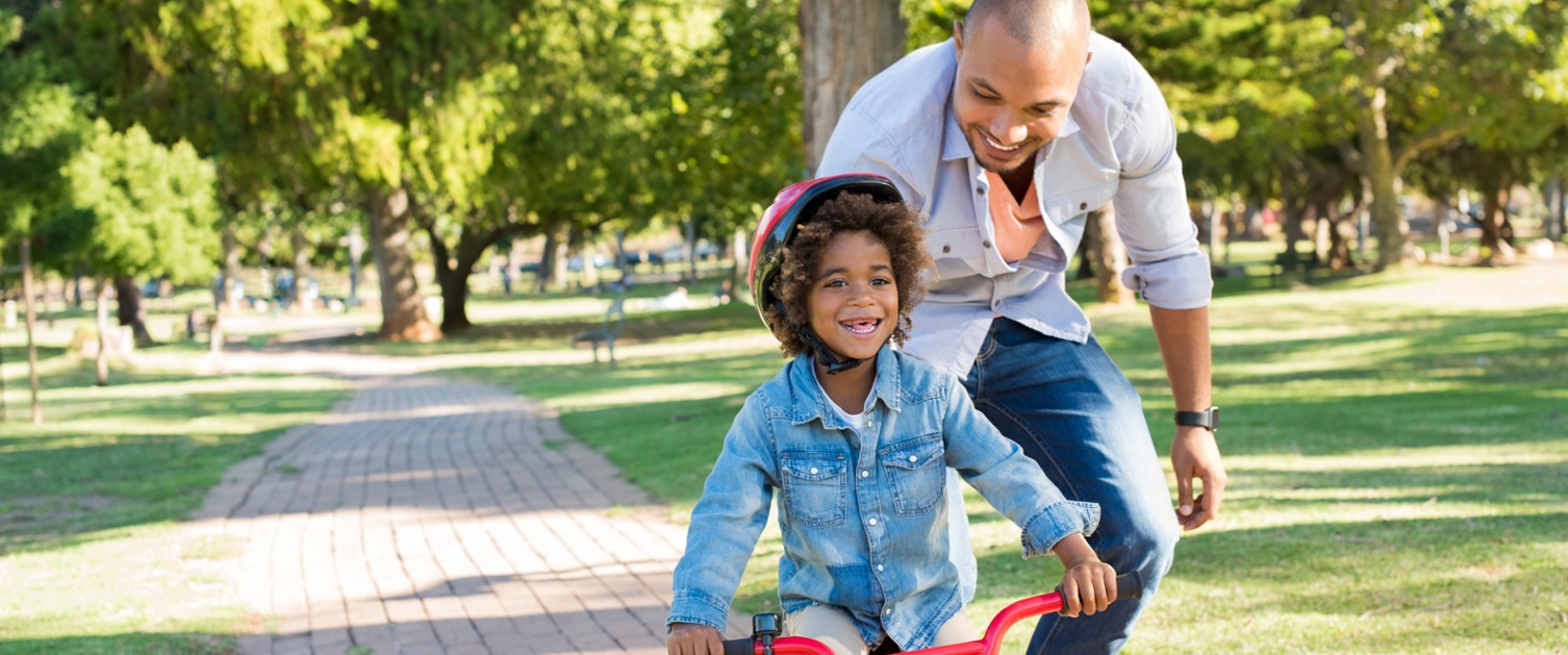 An image of a child on a bike with support from a parent
