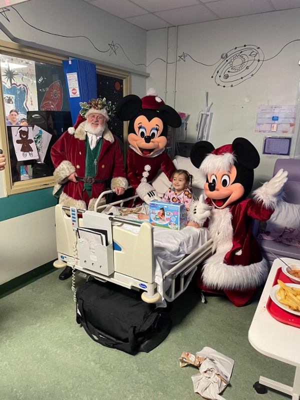 Santa, Mickey and Minnie Mouse with a smiling child in a hospital bed