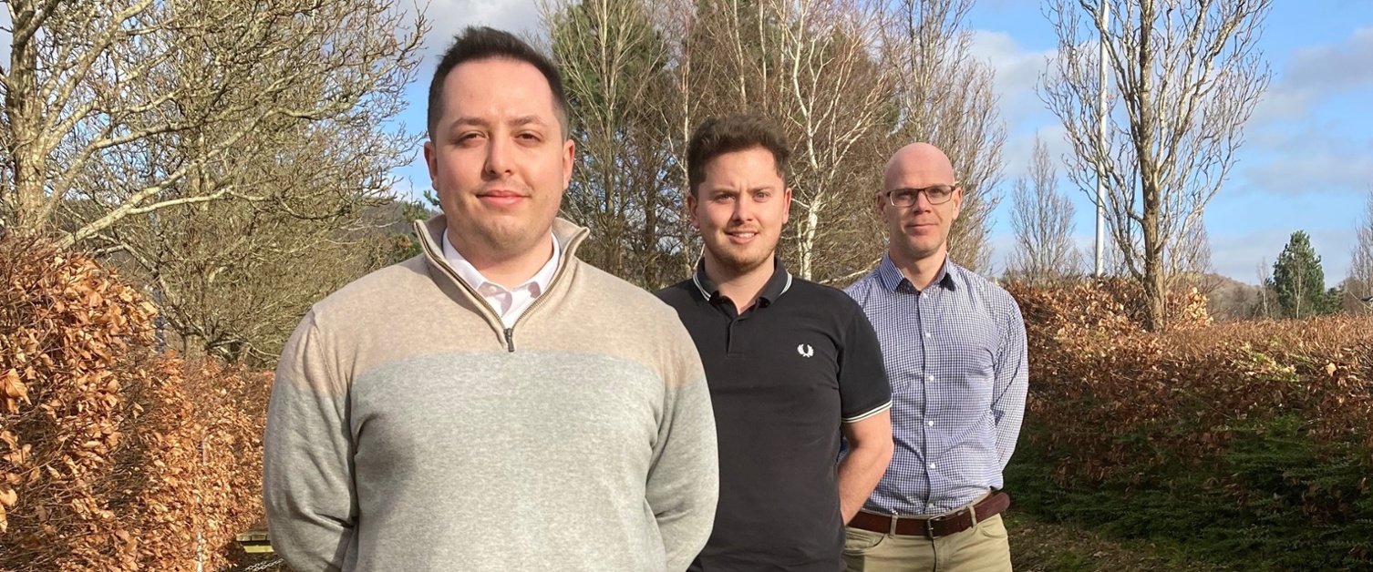 Image shows three men standing in a line