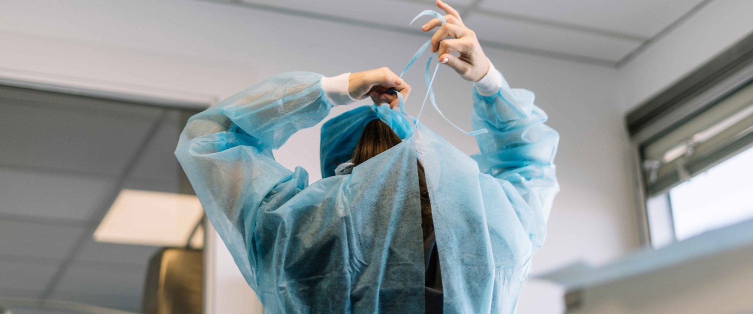 Image shows a surgeon from behind tying their gown at the neck.