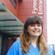 Image shows a nurse smiling into the camera outside a hospital building