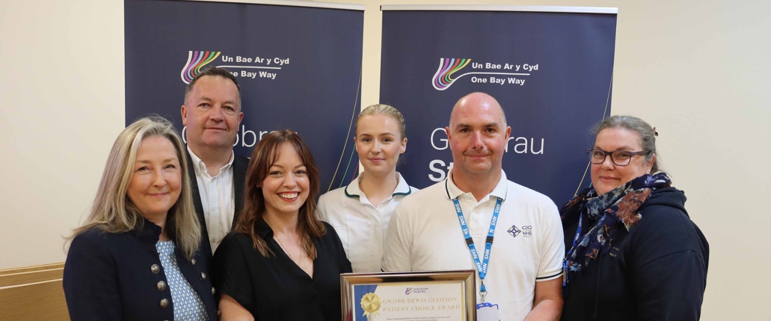 A group smiles at the camera, with two people holding a certificate