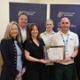 A group smiles at the camera, with two people holding a certificate