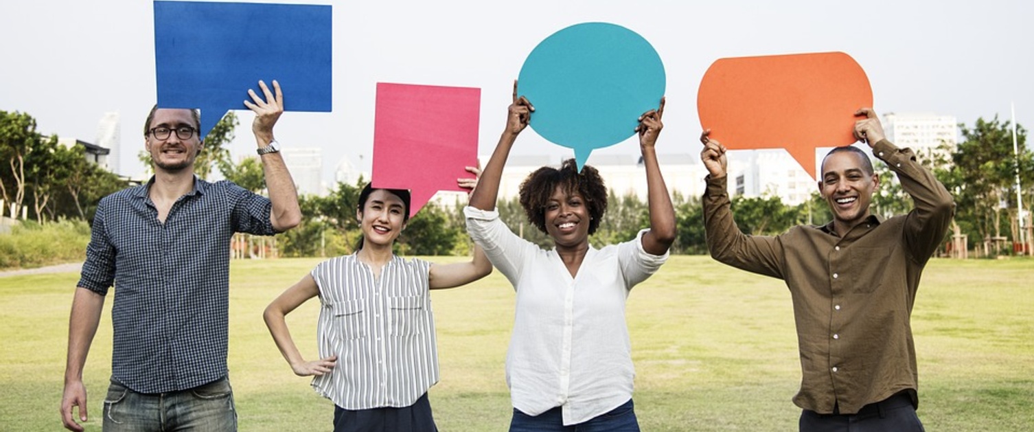 Picture of four people holding up pieces of paper in the shape of speech bubbles.