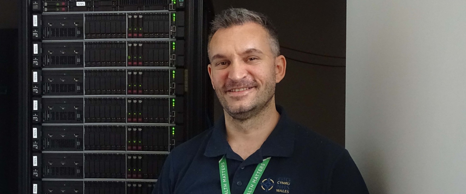 Image shows a man standing alongside a stack of computer servers.