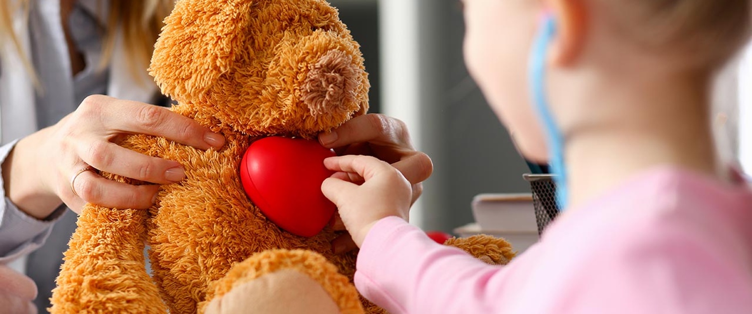 Image shows child with toy stethoscope playing with teddy bear.