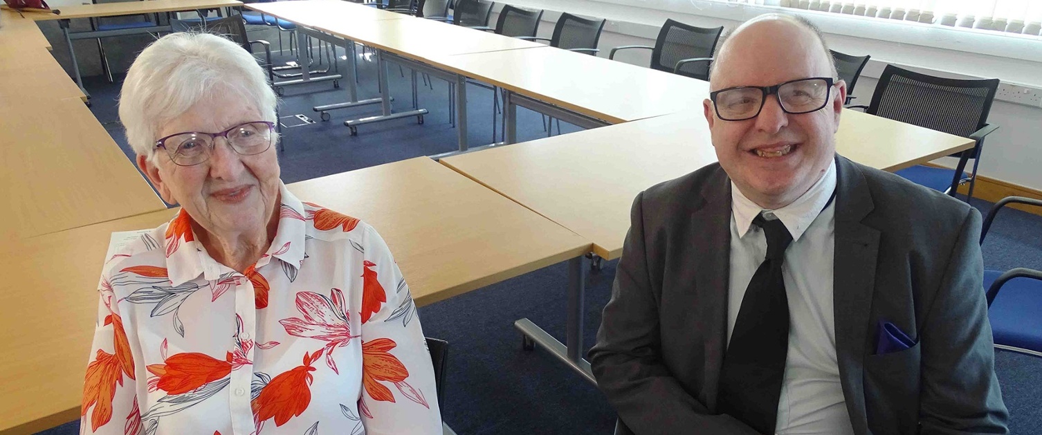 Image shows two people in a meeting room.