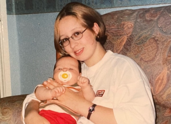 Image shows a young mother holding a baby boy