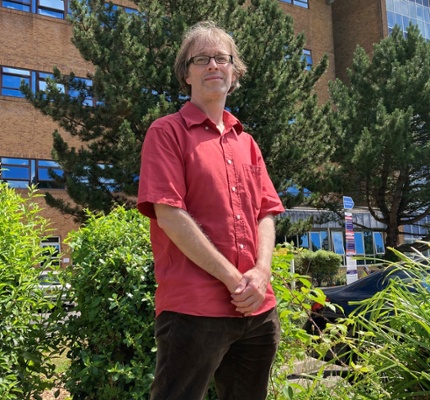 Image shows a man standing in front of a hospital