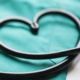 A stethoscope lying on green scrubs makes a heart shape.