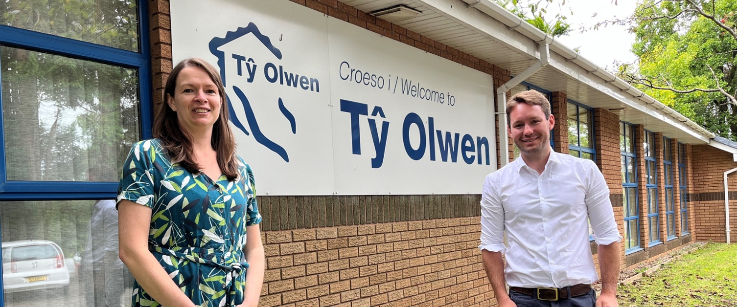 Image shows a woman and man standing in front of a sign