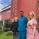 Image shows a man and two women standing outside a hospital