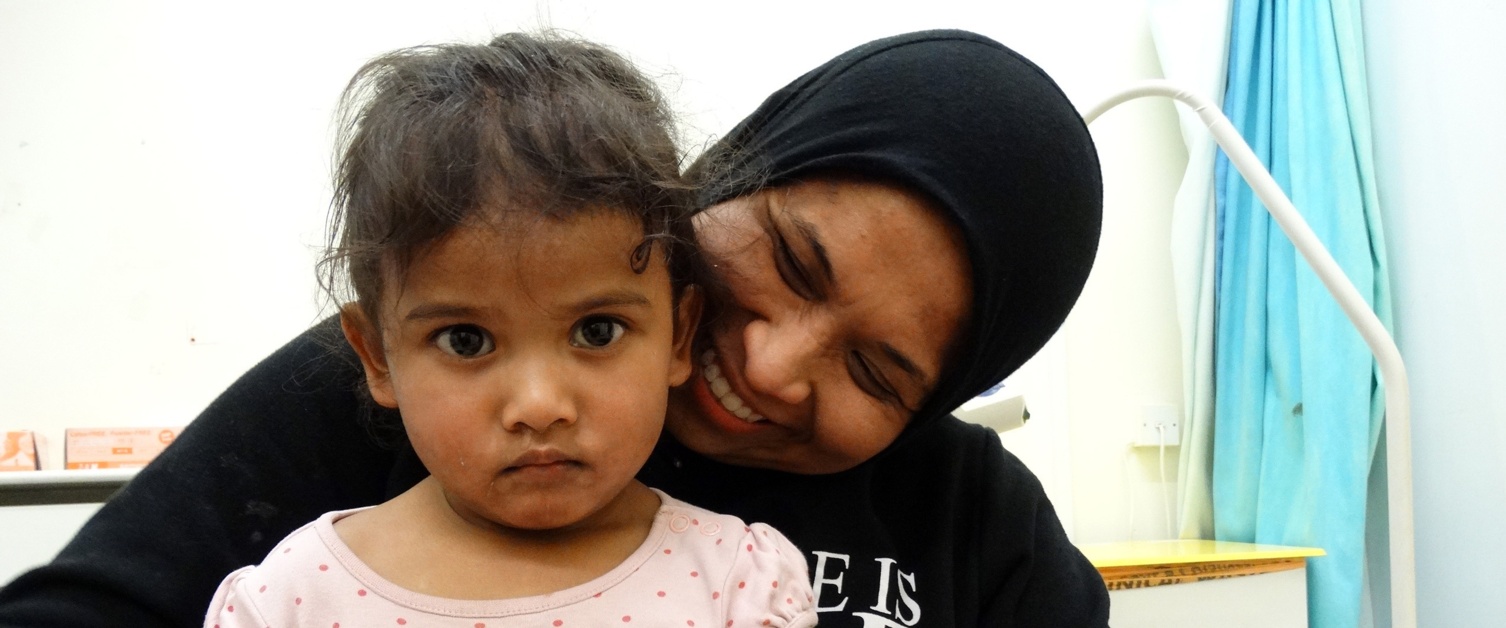 A toddler who has just had the flu nasal spray sits on her mother