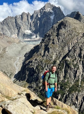 Image shows a man standing in a mountain range