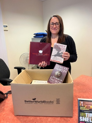 Image shows a woman holding books in front of a cardboard box