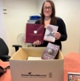Image shows a woman holding books in front of a cardboard box