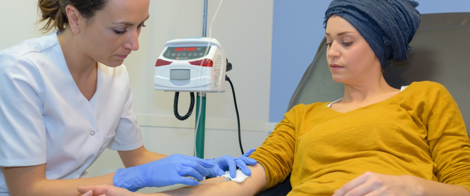 A patient on a reclining bed has a needle inserted into her arm