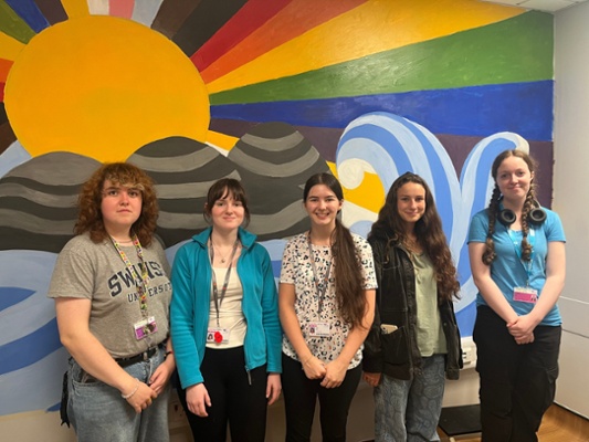 Image shows five women standing in front of a wall