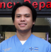 In this profile image, a man wearing pale blue scrubs stands in front of the emergency department entranceway at Morriston Hospital.