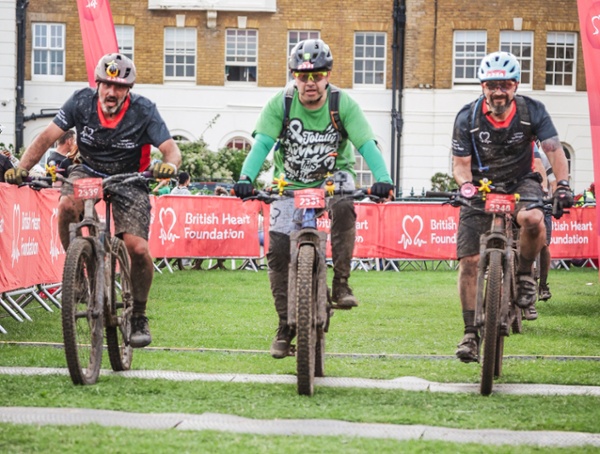 Three men on mountain bikes crossing a finish line