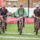 Three men on mountain bikes crossing a finish line