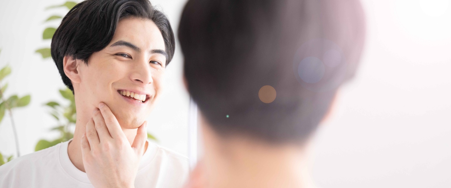 Image of man smiling at reflection in mirror and touching his jaw.