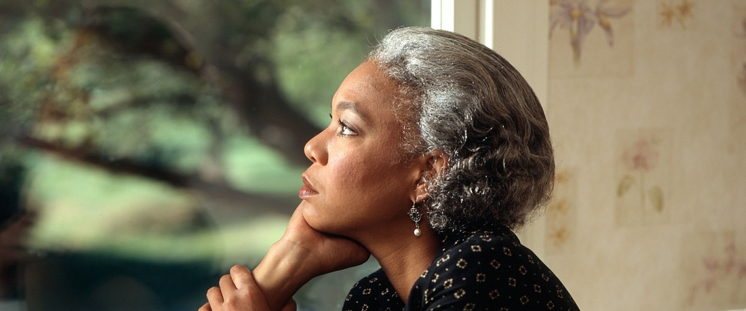 A woman sits alone looking out of a window.