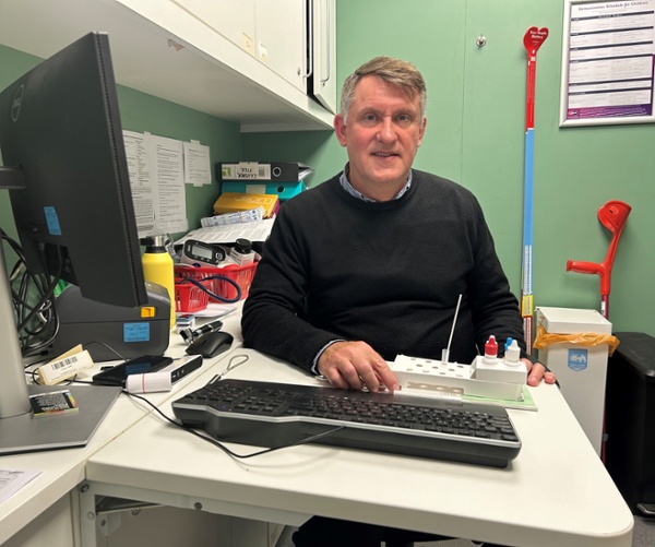 Christopher sat at a desk with the testing kit