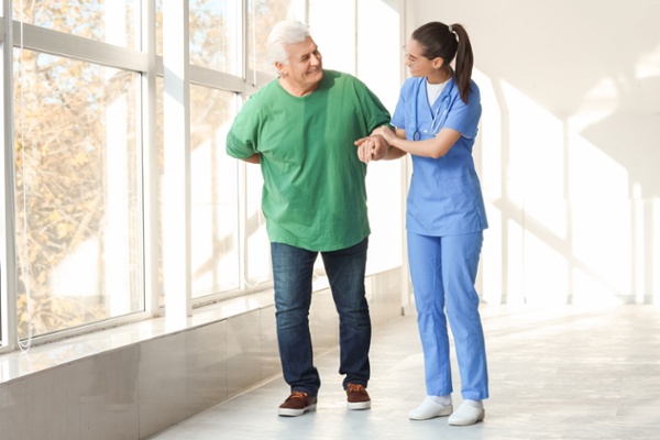 Image shows a man walking with a nurse helping him