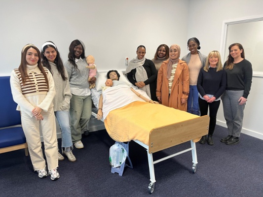 Image shows a group of women standing around a hospital bed