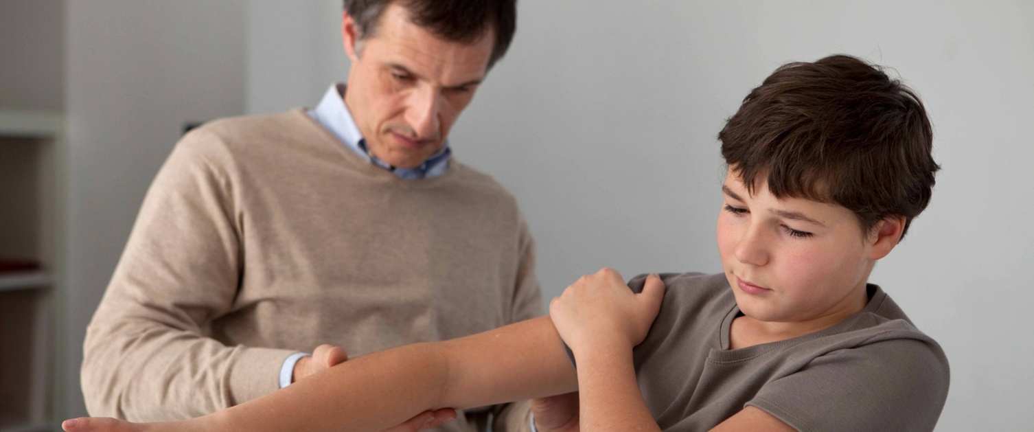 Image shows a doctor examining the arm of a young boy.