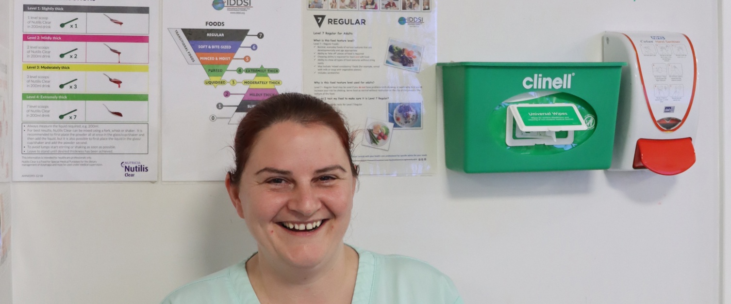 A member of hospital catering staff standing in front of a notice board covered in information about dysphagia