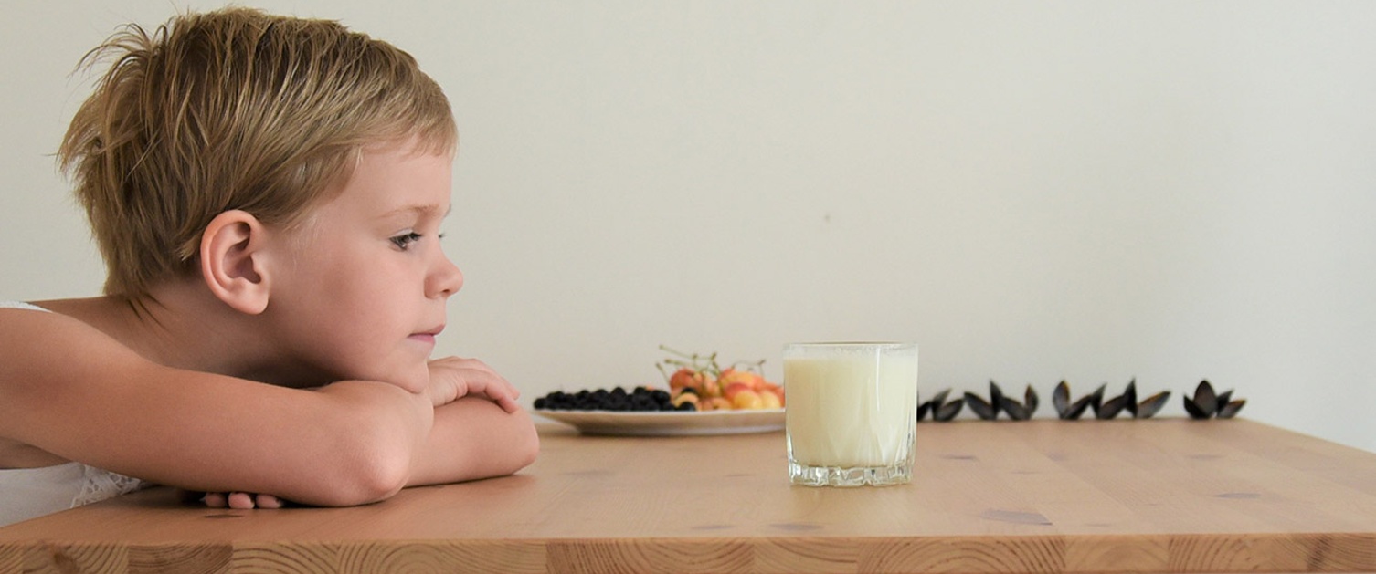 Image shows young child with head on table looking at glass of milk and nuts.