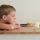 Image shows young child with head on table looking at glass of milk and nuts.