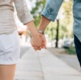 A couple walking along a pavement holding hands.