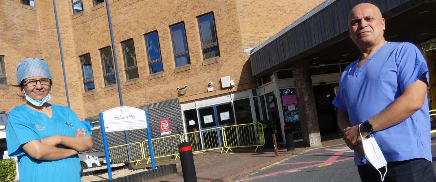 Image shows two clinicians in scrubs outside a hospital building