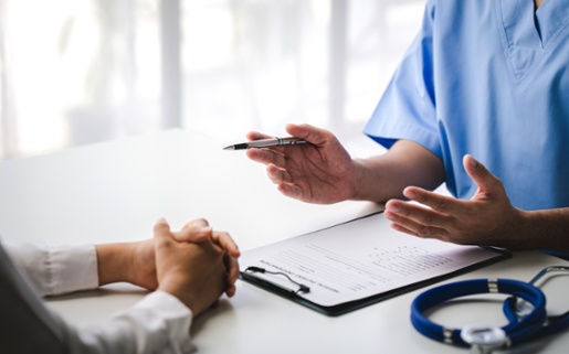 Image shows a patient's hands on a table, with a doctor's hands in view opposite.